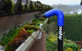 SkyVac hose reaching up into a gutter full of moss along a roof edge